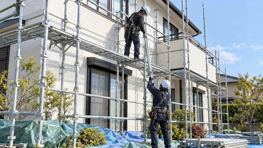 仕上がった外壁の前で部材を手渡しで下ろす足場解体の作業